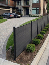 Angled black composite fence installation along a landscaped driveway border