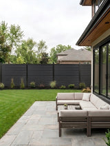 Black composite privacy fence installed around a backyard lawn and patio seating area