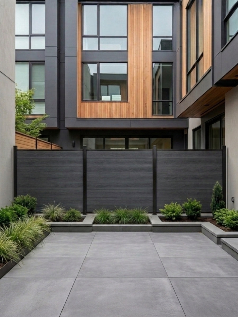 Black composite privacy fence installed in a modern paved courtyard with planters