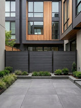 Black composite privacy fence installed in a modern paved courtyard with planters