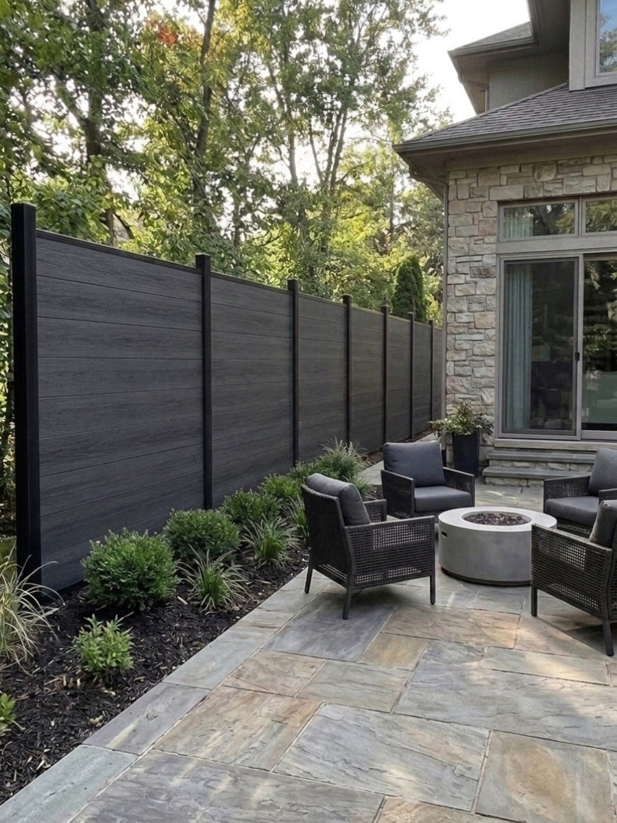 Black composite fence bordering a stone patio with outdoor chairs and a fire pit