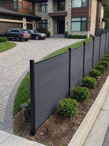 Light gray composite fence installed along a landscaped front yard and curved driveway