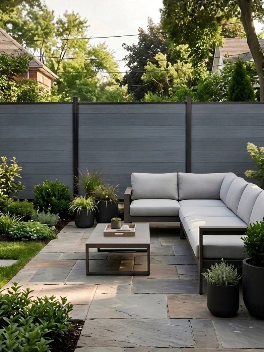 Light gray composite fence surrounding a landscaped patio with sectional sofa and coffee table
