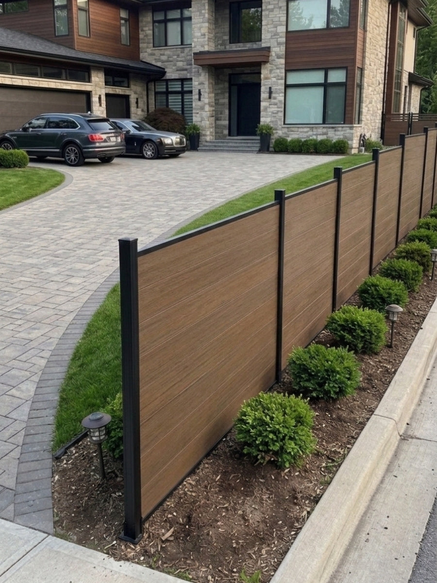 Angled walnut composite fence installed along a driveway with shrubs and black posts