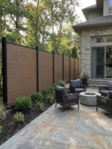 Walnut co-extrusion composite fence lining a stone patio beside a house and fire pit seating