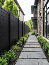 Black aluminum full privacy fence installed along a landscaped walkway beside a modern home