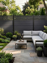 Black top lattice privacy composite fence bordering a garden patio with sectional sofa and coffee table