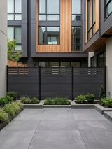 Black composite privacy fence enclosing a paved modern courtyard with raised planting beds