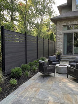 Black top lattice composite fence installed beside a stone patio with outdoor chairs and fire pit