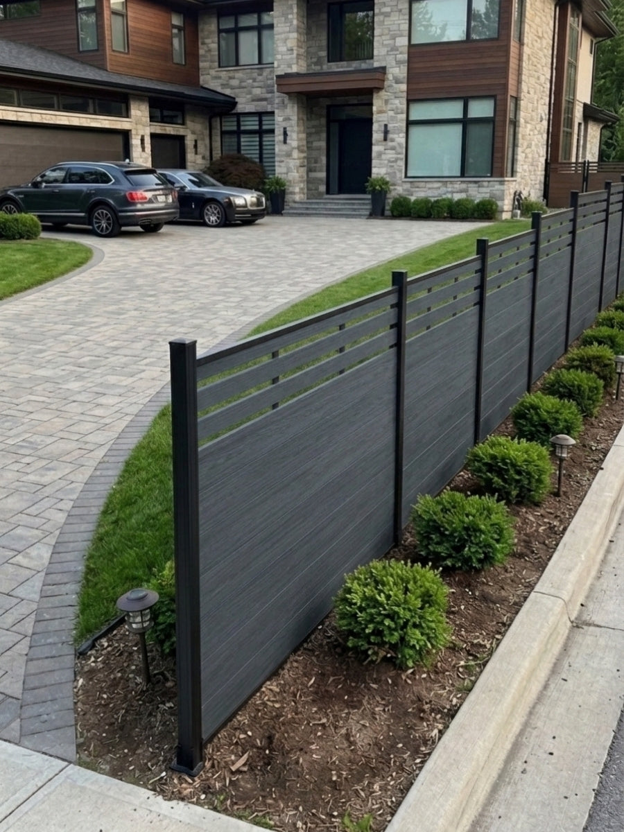 Light gray composite privacy fence with dark posts bordering a landscaped front driveway