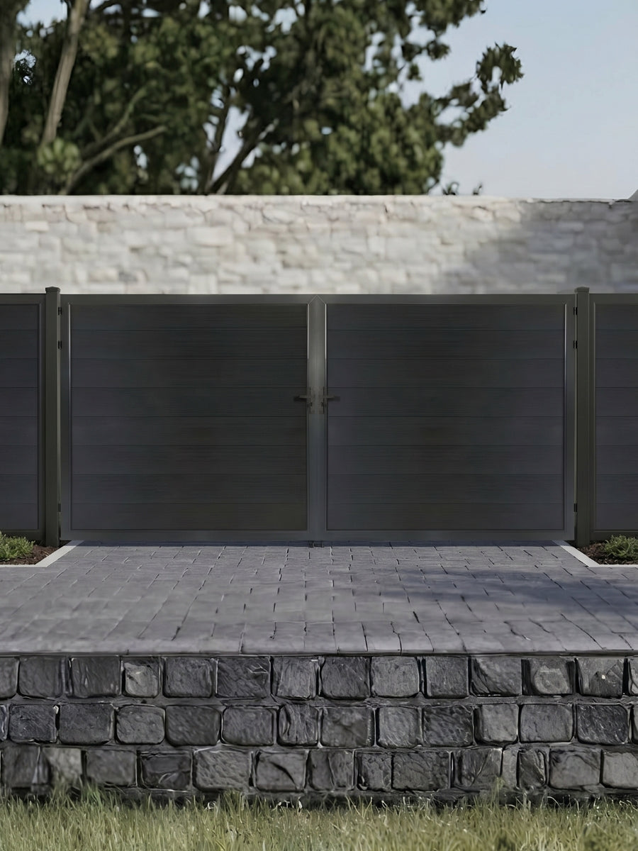 Black WPC double fence gate with horizontal privacy panels installed at a residential driveway with matching fencing and stone retaining wall.