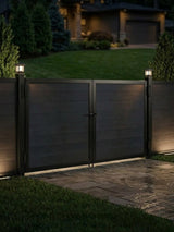 12ft x 6ft black WPC double fence gate with horizontal privacy panels installed at a residential driveway with illuminated gate posts at night.